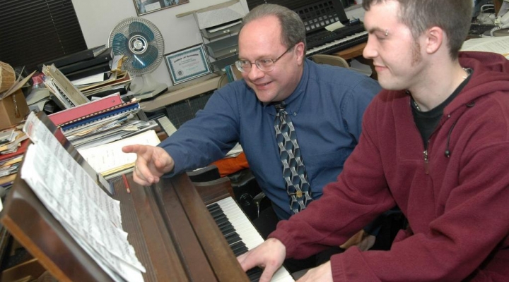 a faculty member teaches a student to play the piano