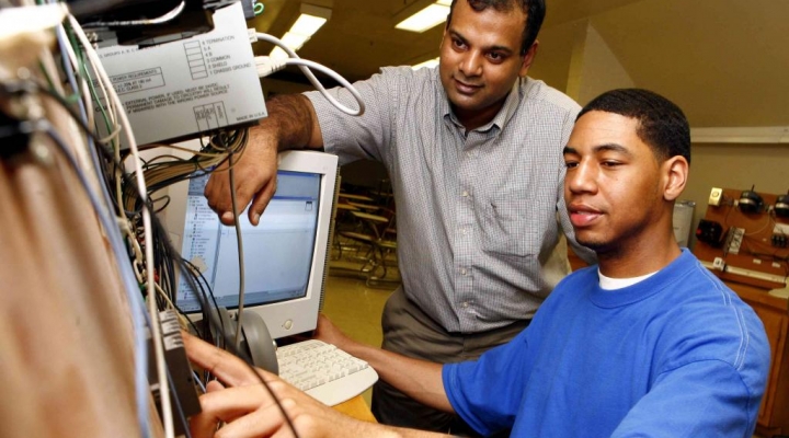 a faculty member shows a student how to operate a machine with a compute